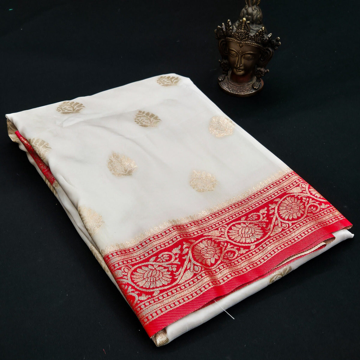 Folded white Banarasi silk saree with red zari border and gold woven motifs